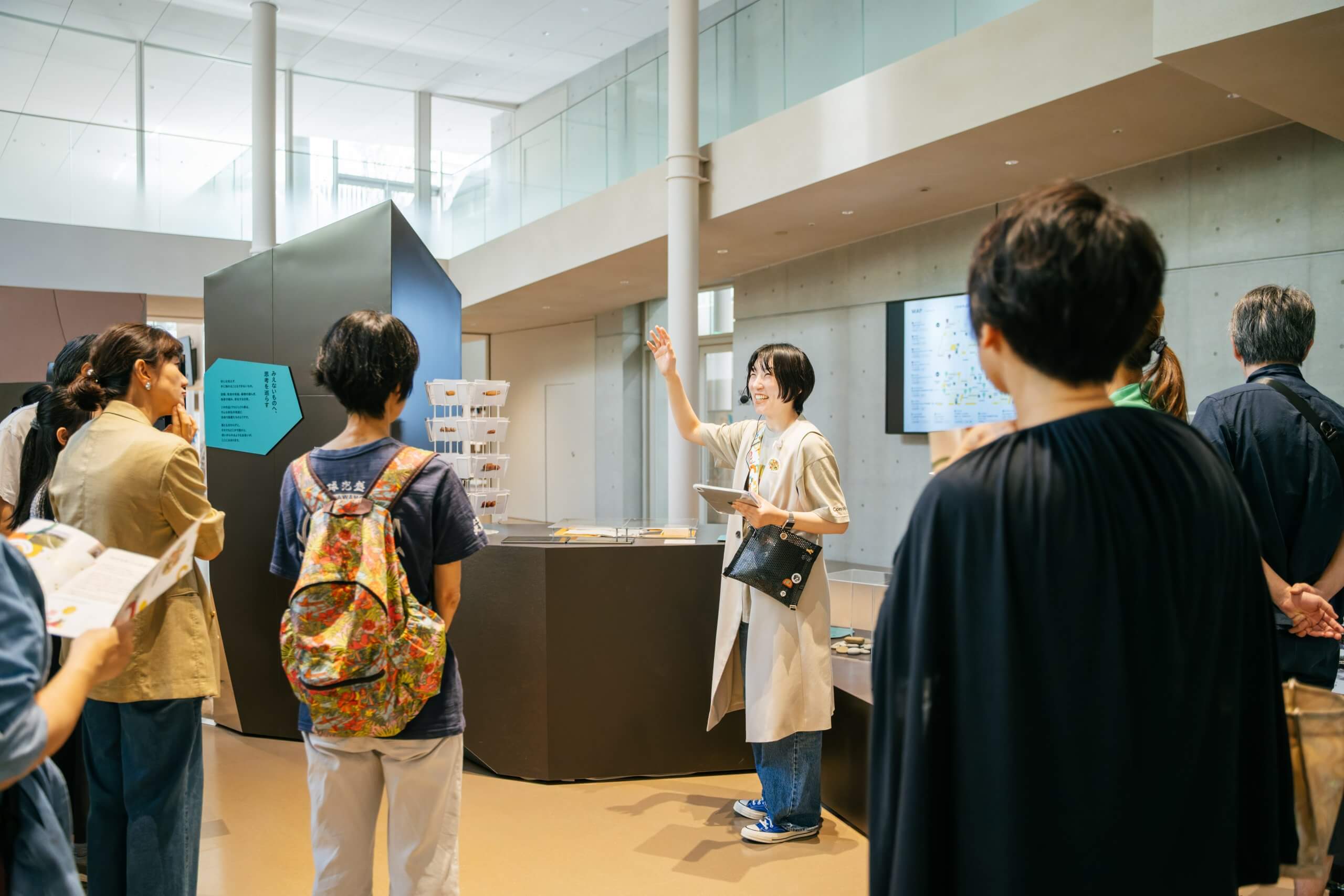 画像：女性スタッフが来館者にツアーをしている様子。スタッフは笑顔で手を上げながら話している。