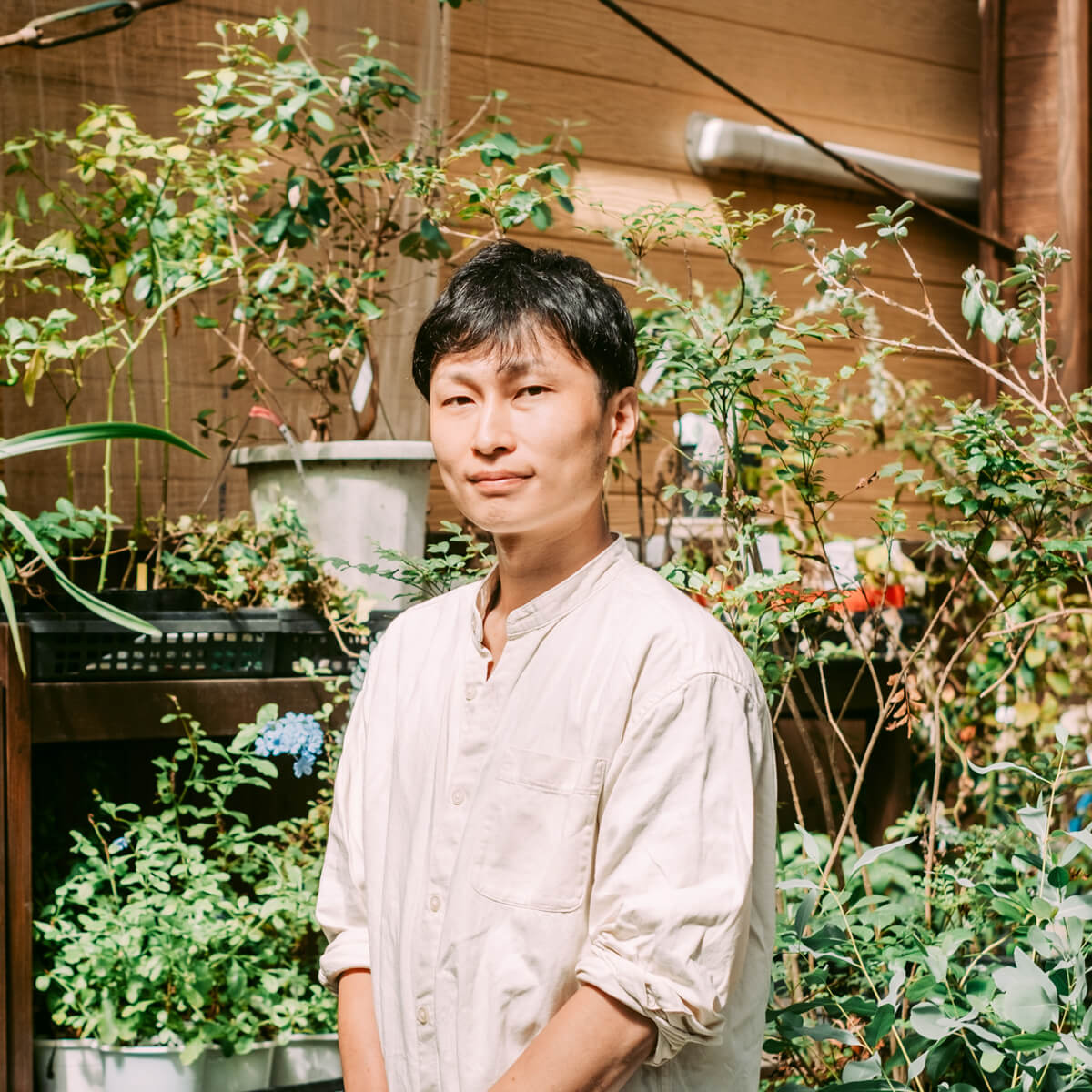 白いシャツを着た男性の写真。植物の前に立っている