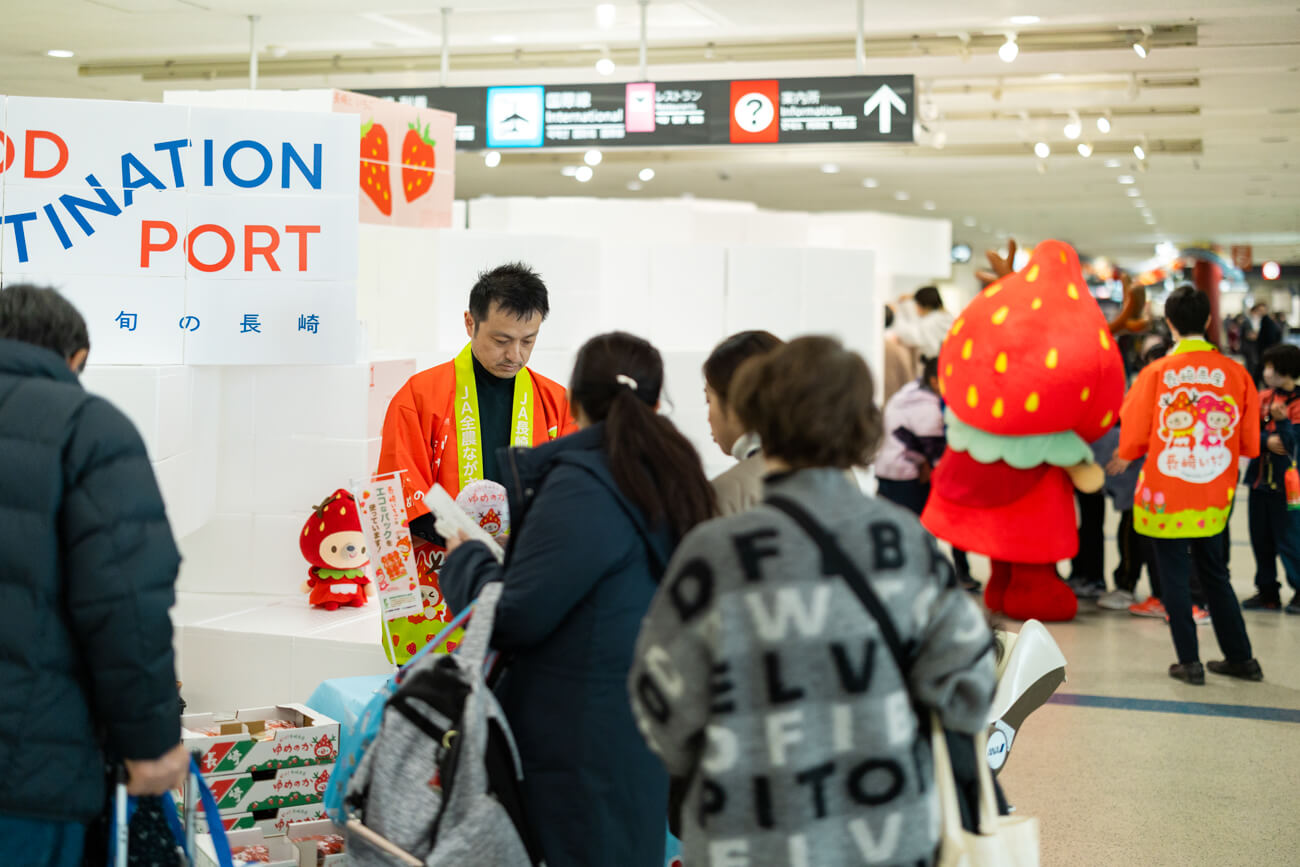 空港ロビーでいちごの即売会が行われている様子。赤いハッピを来た県職員が、ブースに並んでくれたお客様たちにいちごを手売りしている