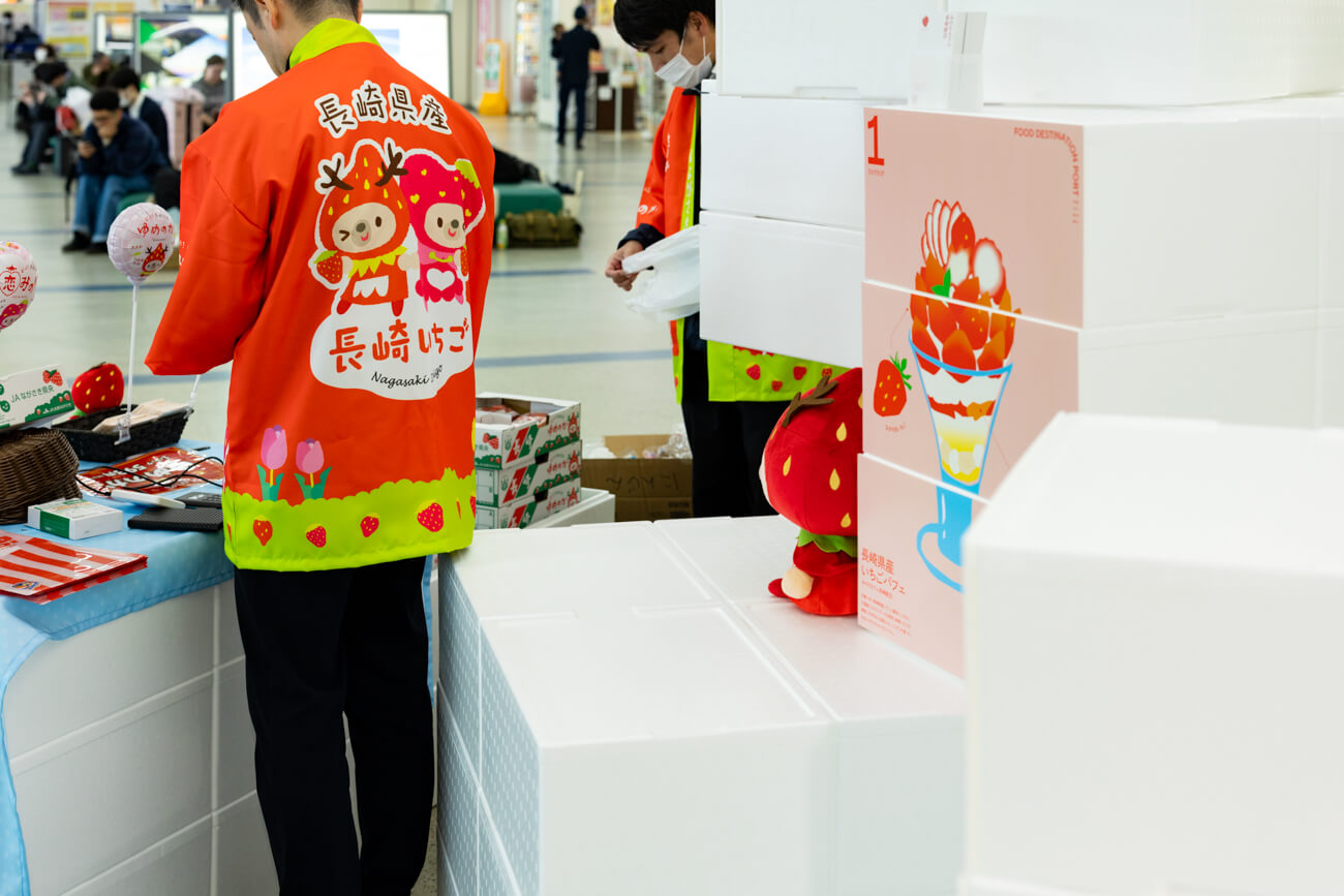 空港ロビーでいちごの即売会が行われている様子。赤いハッピを来た県職員が、ブースに並んでくれたお客様たちにいちごを手売りしている