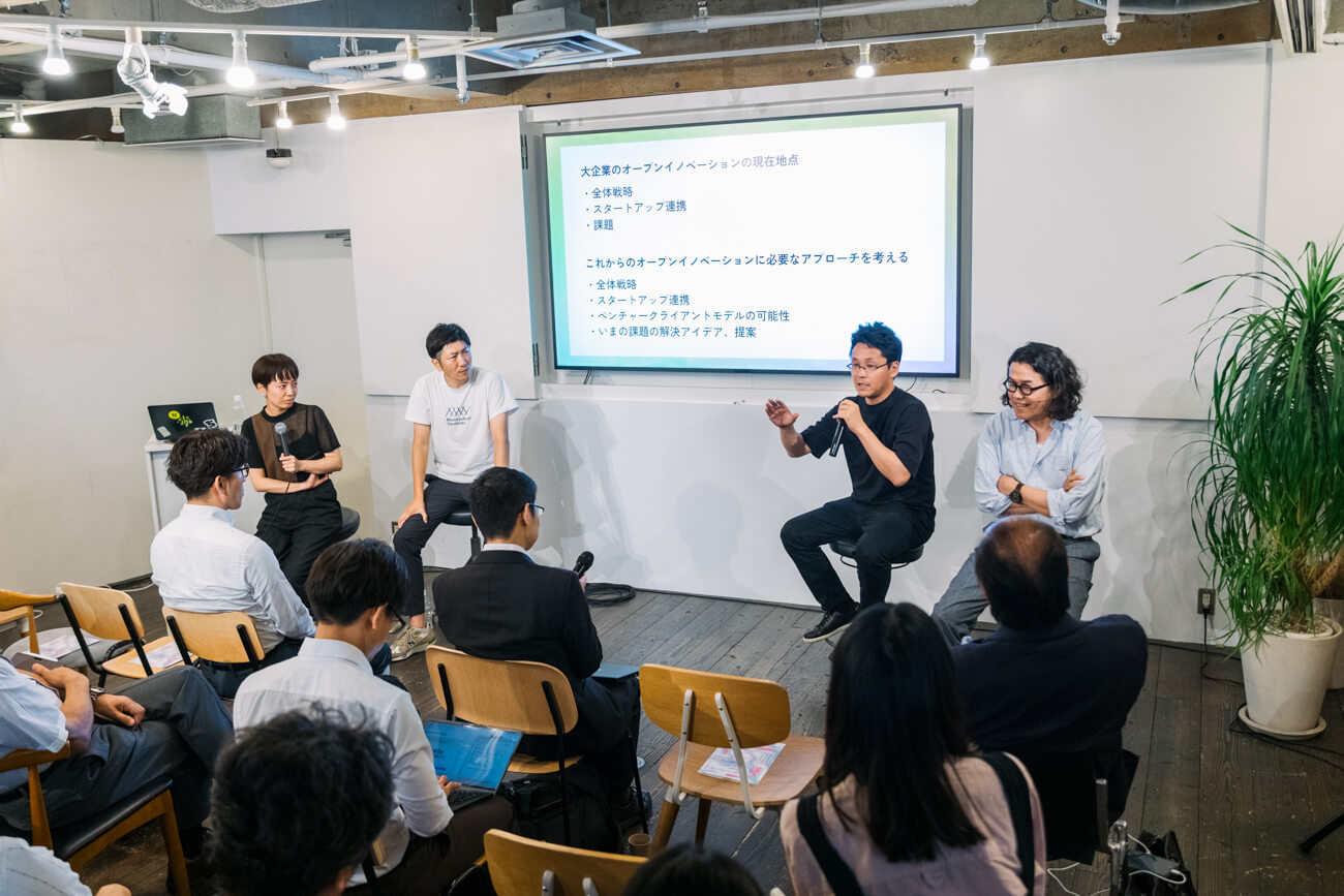 登壇者たちがディスカッションをしている様子の写真。多くの参加者がその議論を見守っている