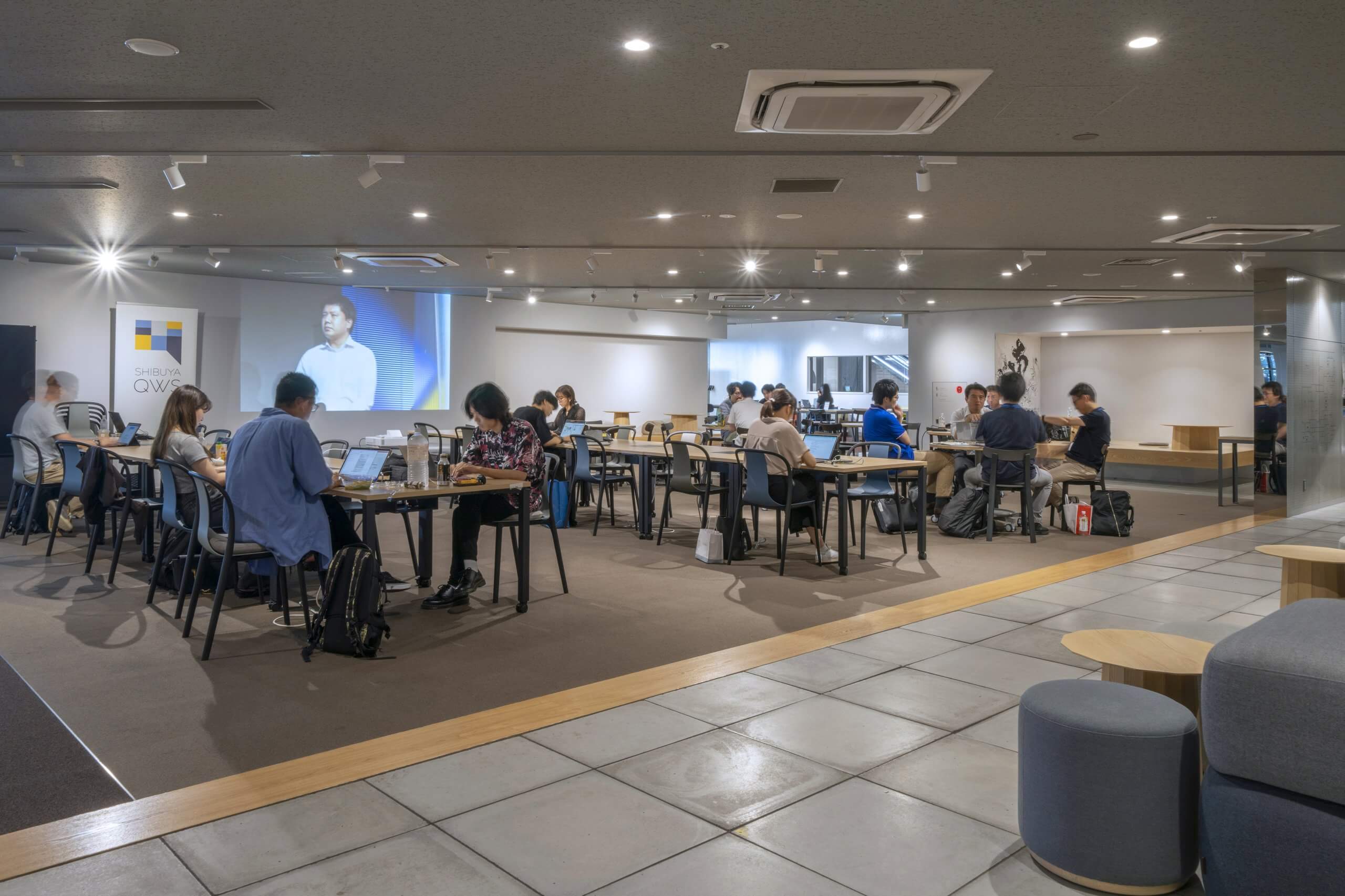 QWSのクロスパークの風景。仕事をしている人が多数。モニターには映像が投影されている。