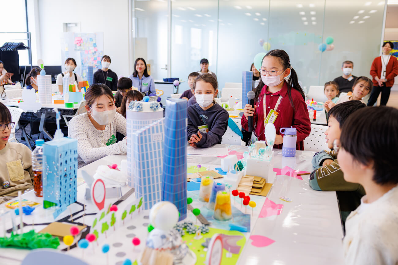 子どもたちが机を囲んでいる様子。机の上には、ワークショップで制作された街の模型が置かれている