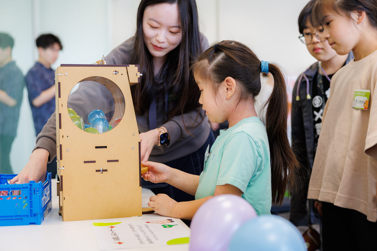 机の上に置かれたガチャガチャの機械を、子どもが操作している様子