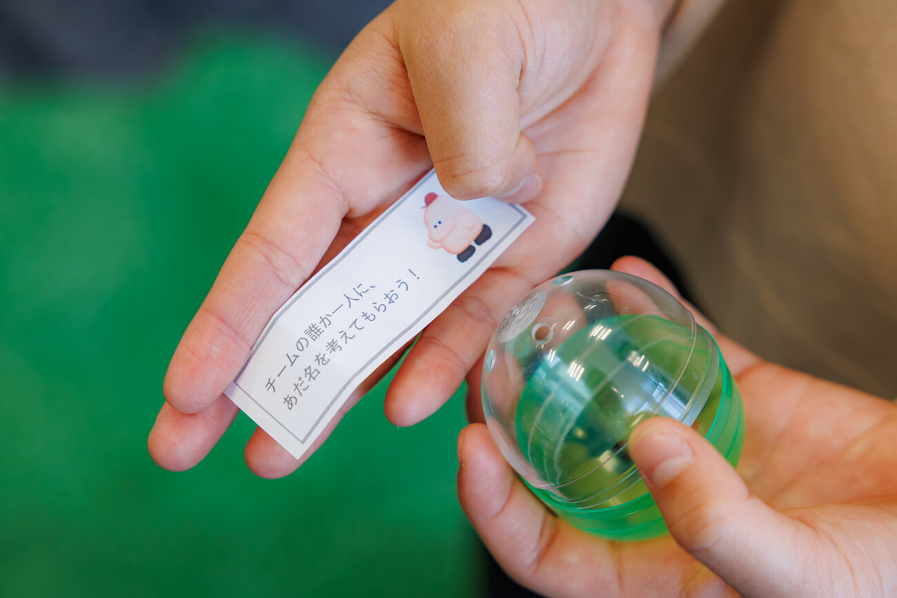 ガチャガチャのカプセルと、その中に入っていた紙を見せてくれる手元の様子