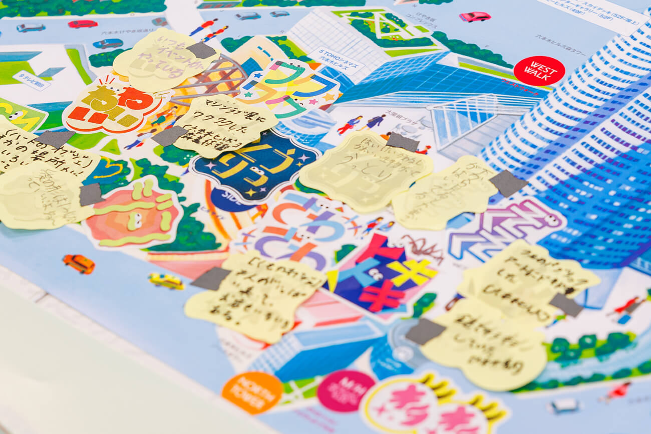 ワークショップで使用された、ワークシートの写真。まちのイラストが書かれた紙の上に、子どもたちが書いたポストイットのメモ書きや、シールが貼られている