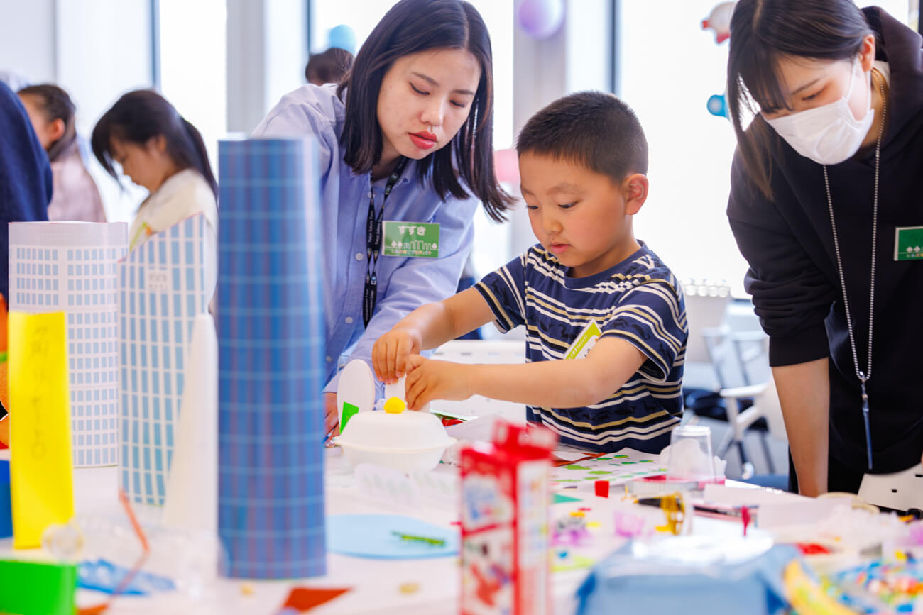 ワークショップに参加した子どもが、まちの模型を制作している様子。近くでは、ワークショップを運営する大人が作業を見守っている