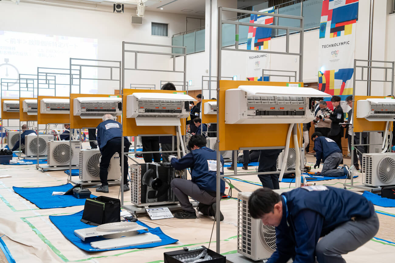 ギノリンピックの会場の様子。撮影された写真には、たくさんのエアコンとそれを修理する技術員たちの姿が写っている