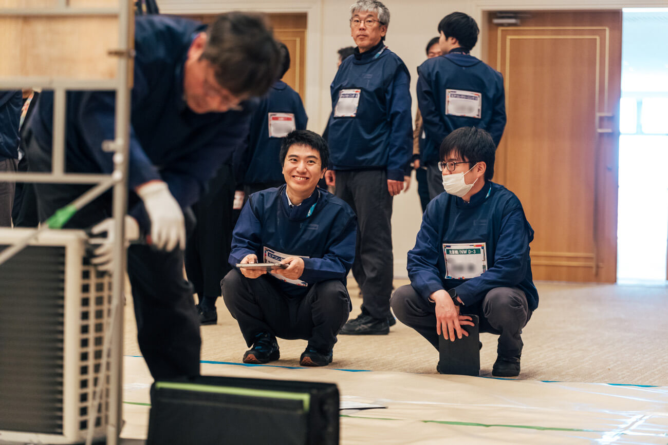 修理技術員を見守る、仲間たちの写真
