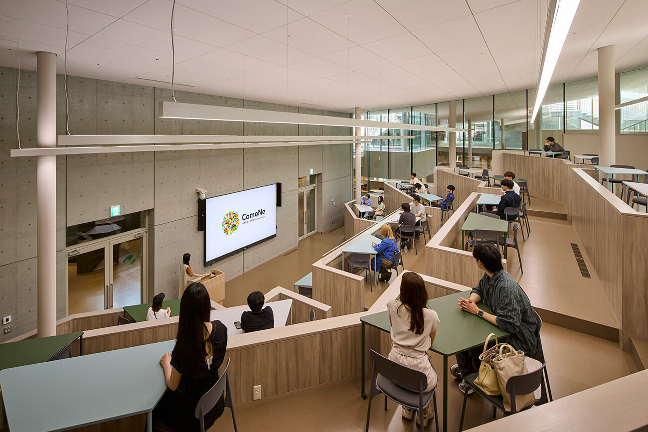『ComoNe』の講義型イベント用スペース。段差状に配置されたテーブル席に参加者が着席し、正面スクリーンで発表者がプレゼンテーションを行っている