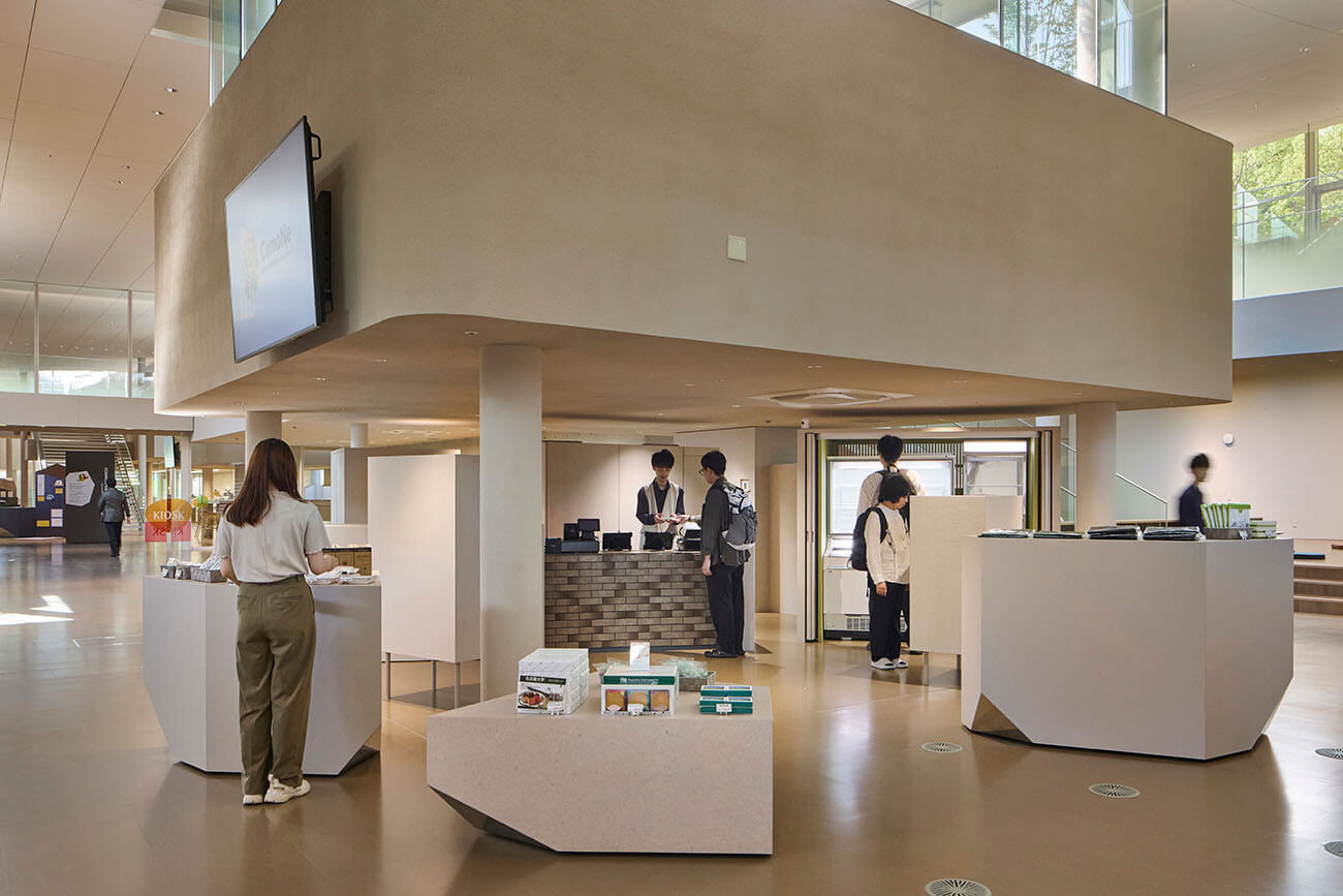 KIOSKエリア（購買エリア）の様子。カウンターでスタッフと来館者がやり取りをし、周囲には商品を並べた什器が配置されている。