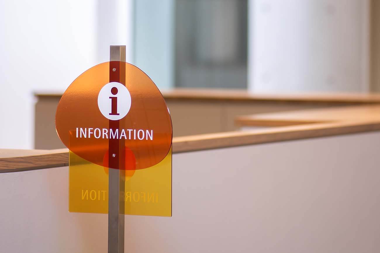 館内に設置されたインフォメーションサイン。オレンジと黄色の透明パネルに『i INFORMATION』と記されている。
