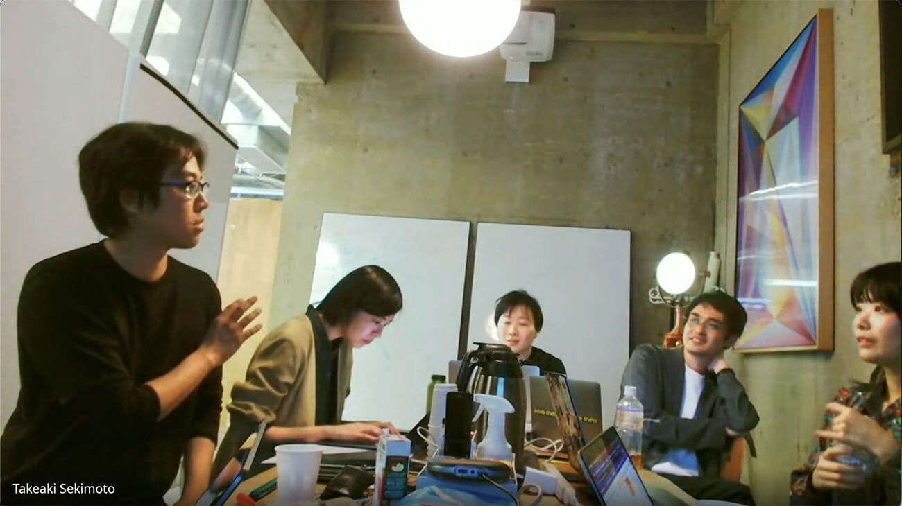 KMDの教員とロフトワークのメンバーが参加する、リブランディングプロジェクトのミーティング風景。ラップトップや資料を囲みながら、和やかながらも活発な議論が交わされている様子。