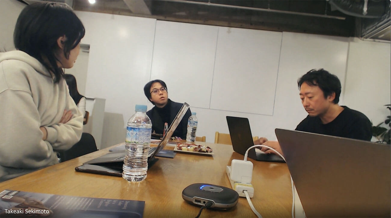 KMDの教員とロフトワークのメンバーがプロジェクトの進行中に行った議論の様子。木製のテーブルを囲み、複数のノートパソコンと資料が置かれている。