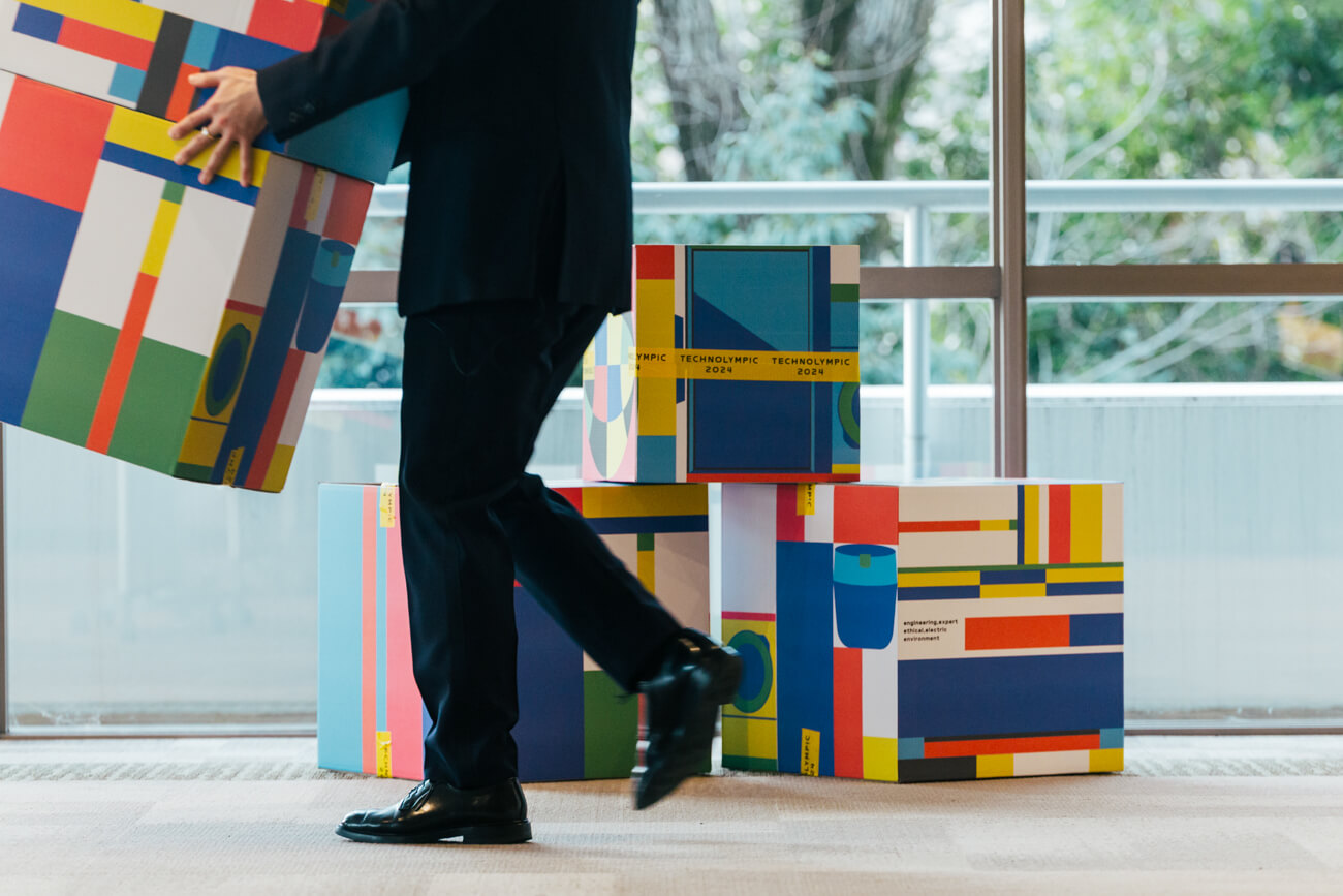 キービジュアルをアレンジした会場装飾の写真。ブロック状になった会場装飾のモチーフを、係の男性が運んでいる