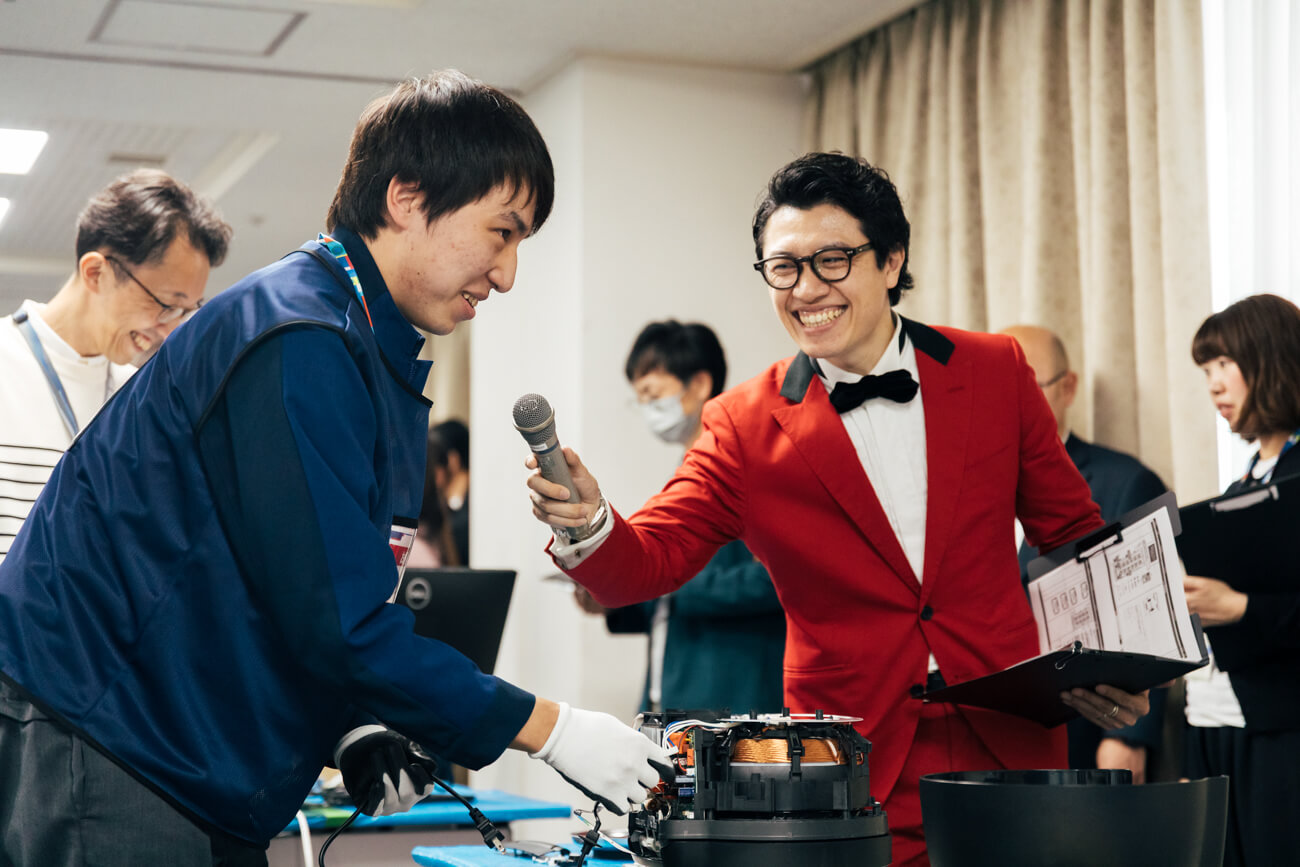 赤いスーツを着た、司会のMCあまり氏が競技の参加者にマイクを向けている様子