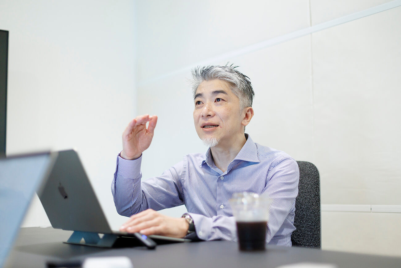 会議室でノートパソコンを前に、諏訪光洋が身振りを交えて説明している様子