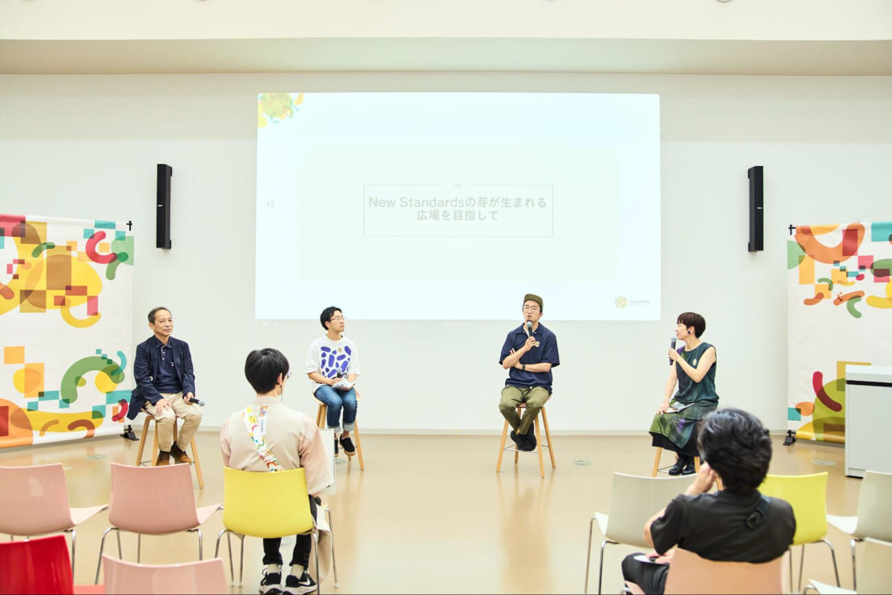 ４人の登壇者が、イベント会場の前に整列して椅子に座っている様子