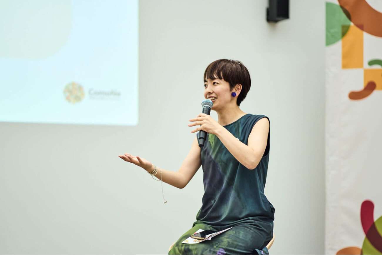 登壇者の女性がマイクを持って壇上で話している様子。明るい表情をしている