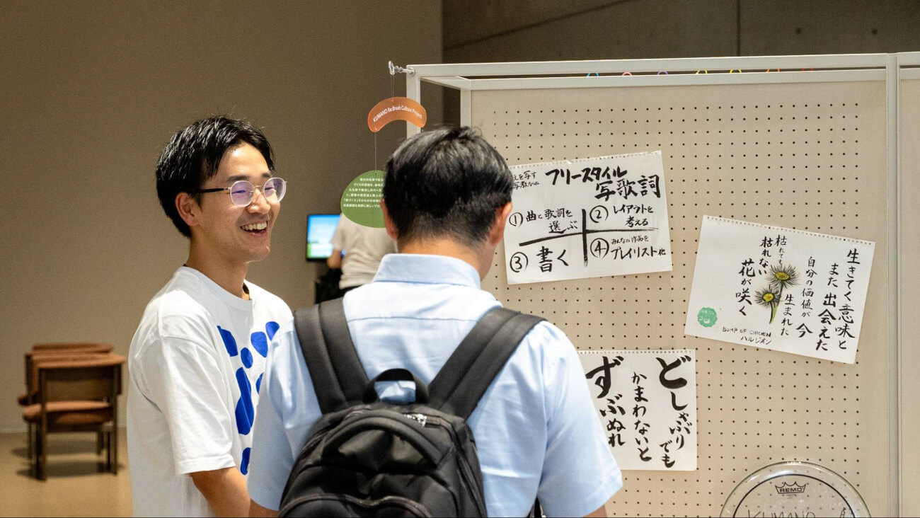 イベントにも登壇した西村さんが、展示用パネルの前に立ち、男性の来場者に対してプロジェクトの説明をしている様子