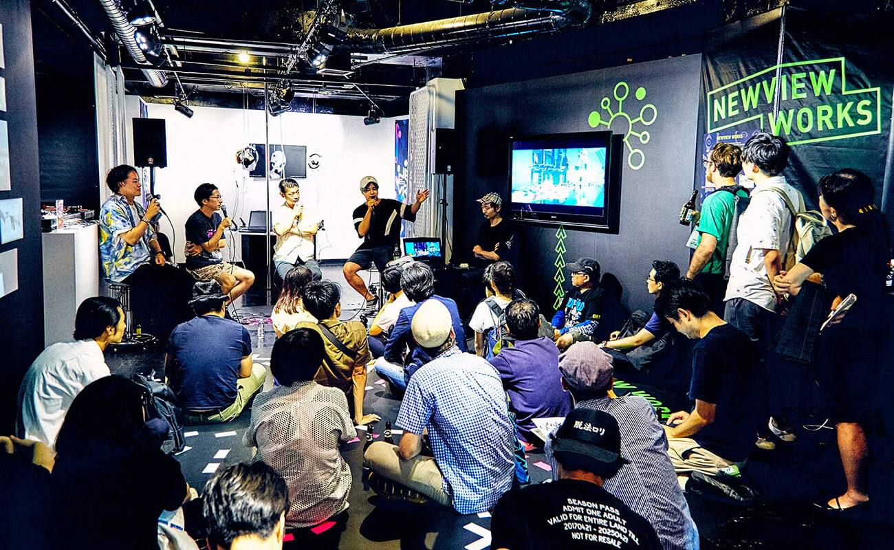 NEWVIEWプロジェクトのイベントで、登壇者がマイクを手に語り、観客がスクリーンを見ながら耳を傾けている様子