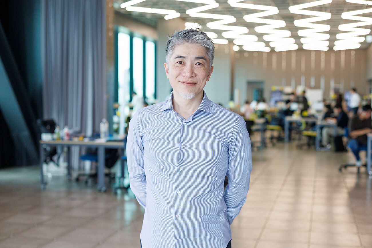 明るいオフィス空間で、諏訪光洋がカメラに向かって立ち、微笑んでいるポートレート