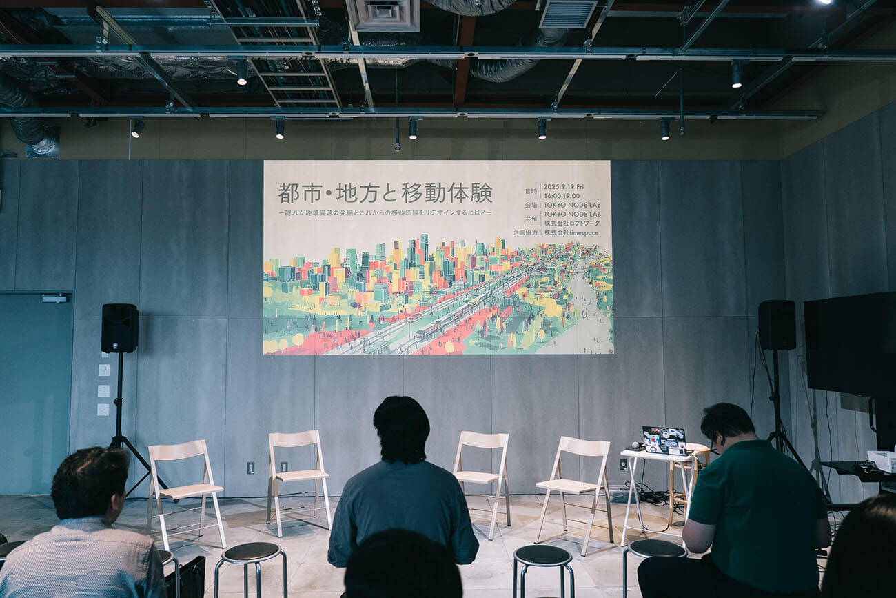 イベント開始前の会場の様子。中心にはイベントのカラフルなビジュアルが投影され、手前にはイベント開始を待つ参加者たちの後ろ姿が見える。