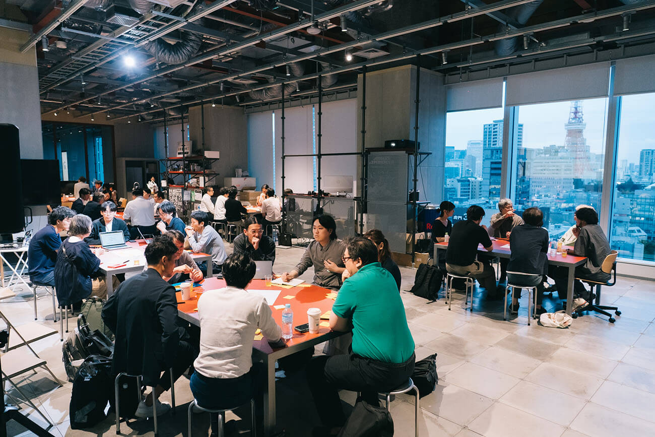 オープンディスカッションの様子。5〜6人ずつ5つの島に分かれて議論を実施。手元には付箋やペンがあり、リラックスしつつも真剣な議論が行われている様子が窺える。