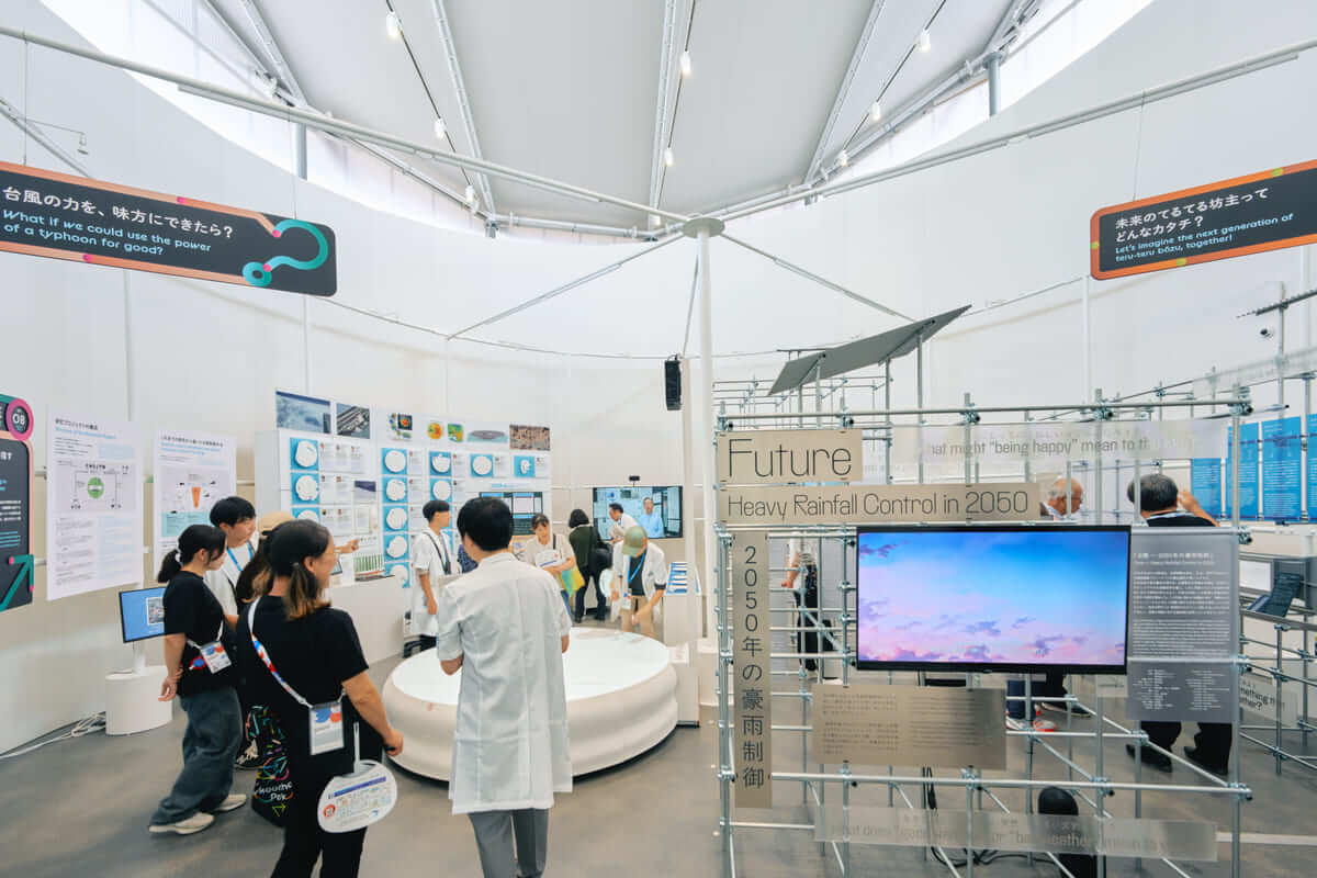 展示会場の写真（中央の円柱から円形に展示用のパイプが広がる様子）