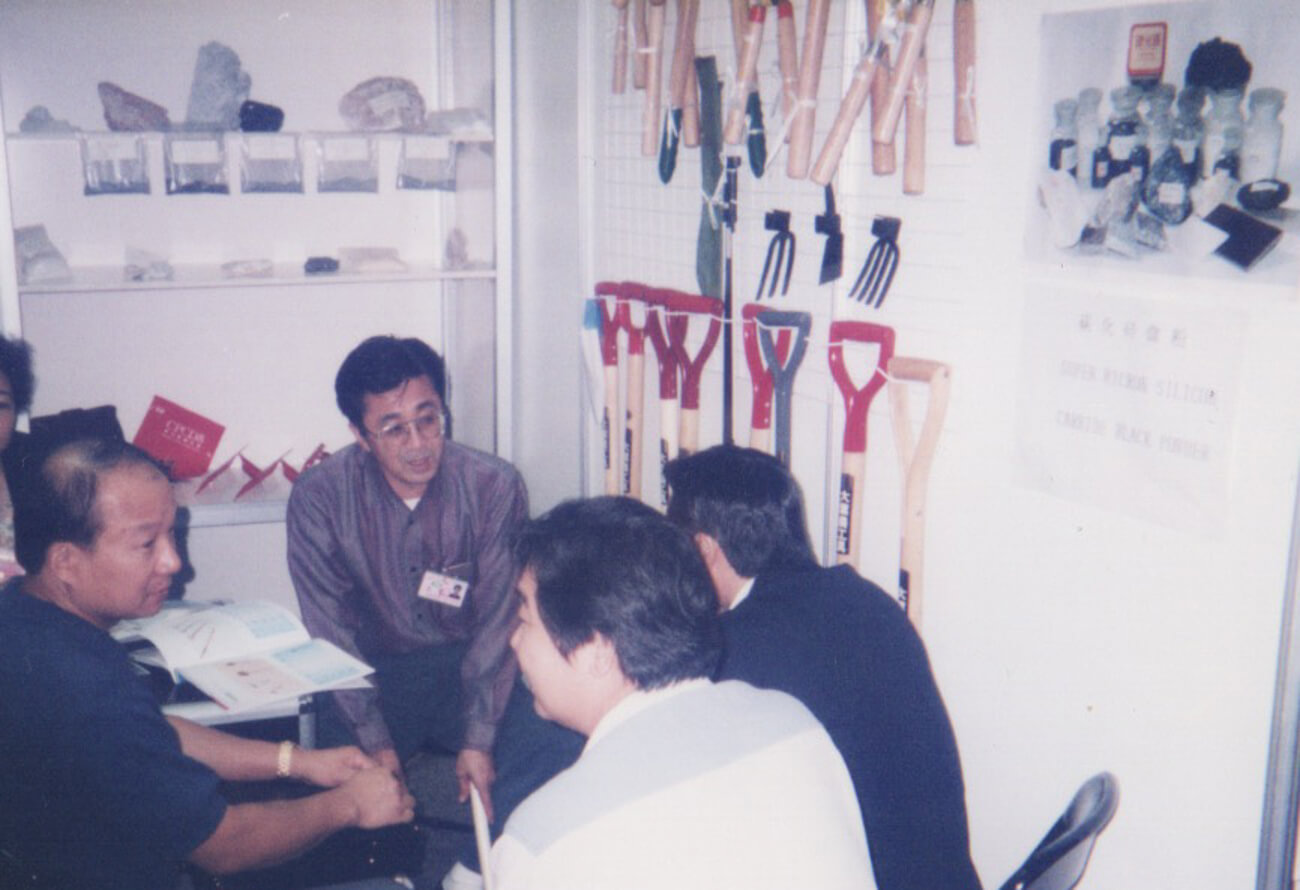 少し色褪せた昔の写真。農業の道具が壁にたくさん吊るされた部屋で、男性4人が話し合っている