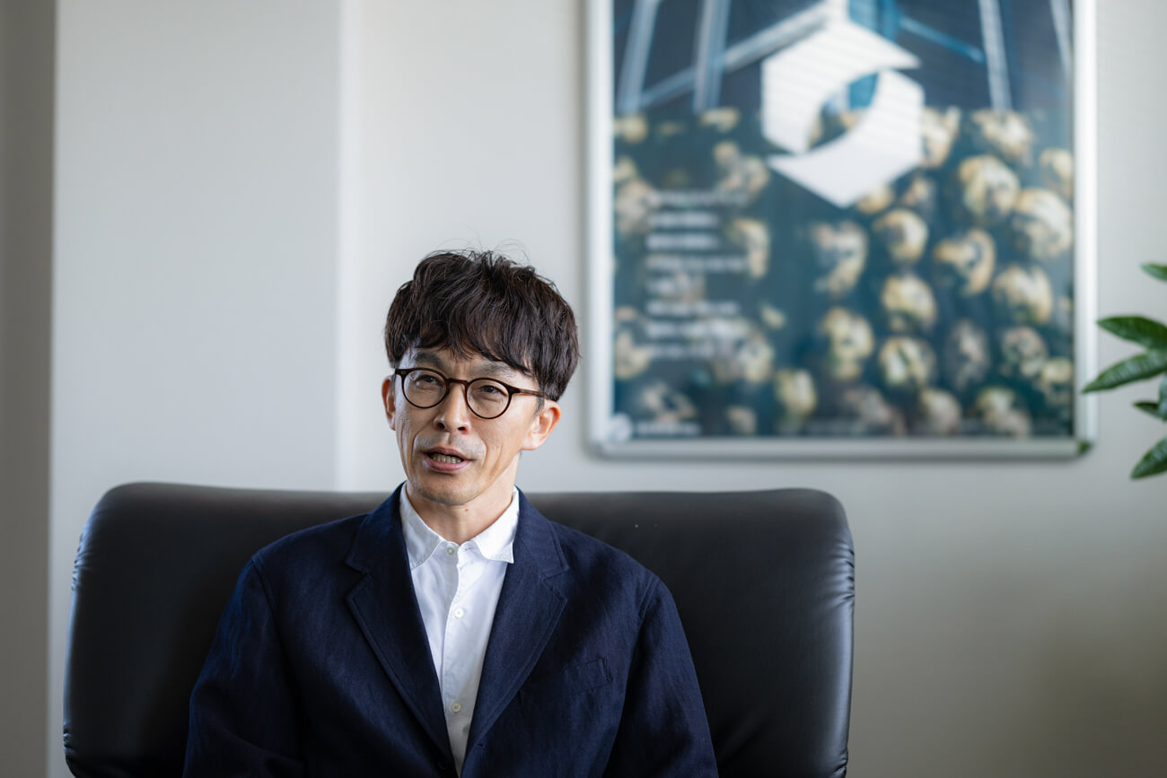 応接室のソファに座った男性が、インタビューに答えている様子