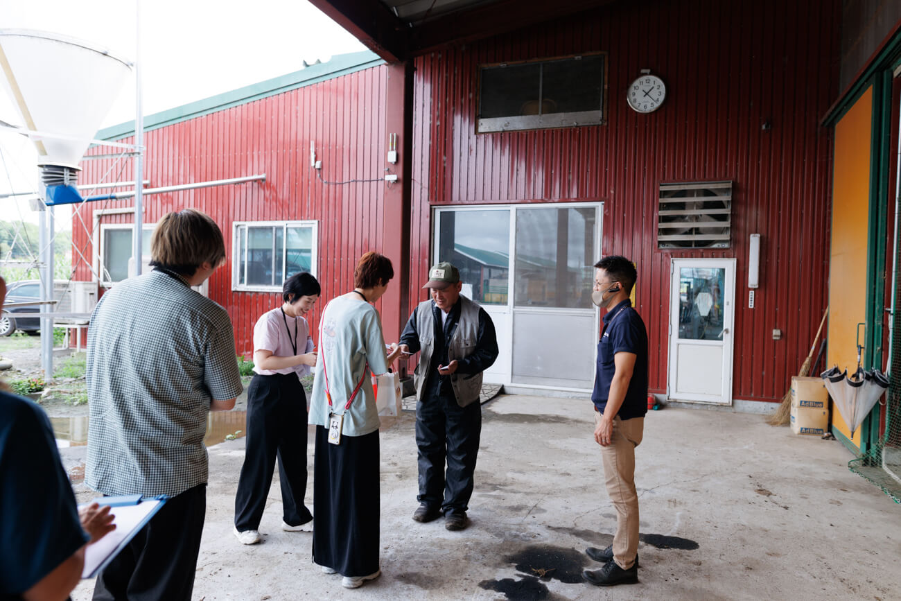 建物の屋根の下で、酪農家の方に挨拶をするロフトワークの面々