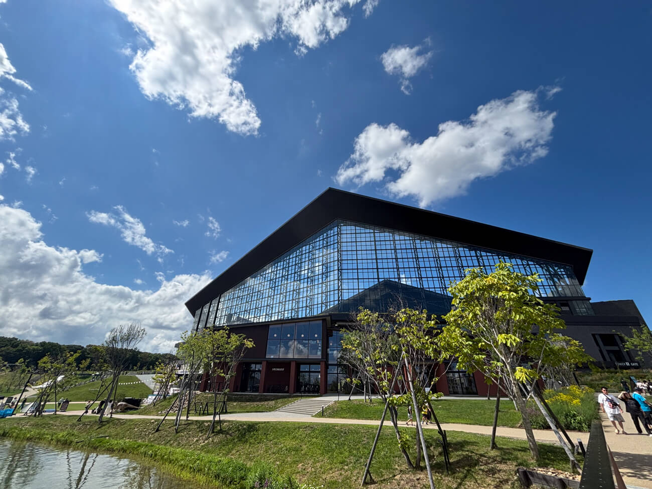 北海道日本ハムファイターズの新球場『エスコンフィールドHOKKAIDO』を含む、新エリア『HOKKAIDO BALLPARK F VILLAGE』の写真。一面ガラス張りの巨大な建築物が、広い公園の中に佇んでいる