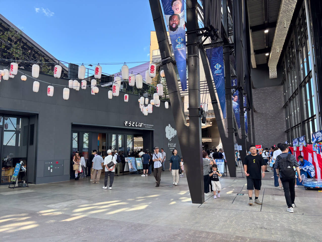  球場『エスコンフィールドHOKKAIDO』の内部の写真。クラフトビール醸造レストランや飲食店が並ぶなかを、来場者の方々が歩いている