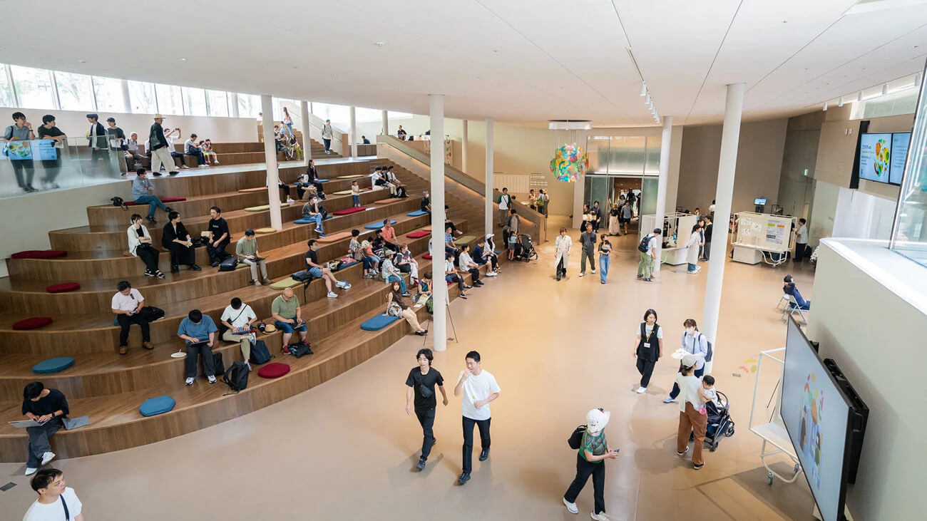 「Common Nexus（愛称：コモネ）」のロビーの写真。広い通路のはしには大きな階段上のスペースがあり、多様な人がそこに座って思い思いの時間を過ごしている
