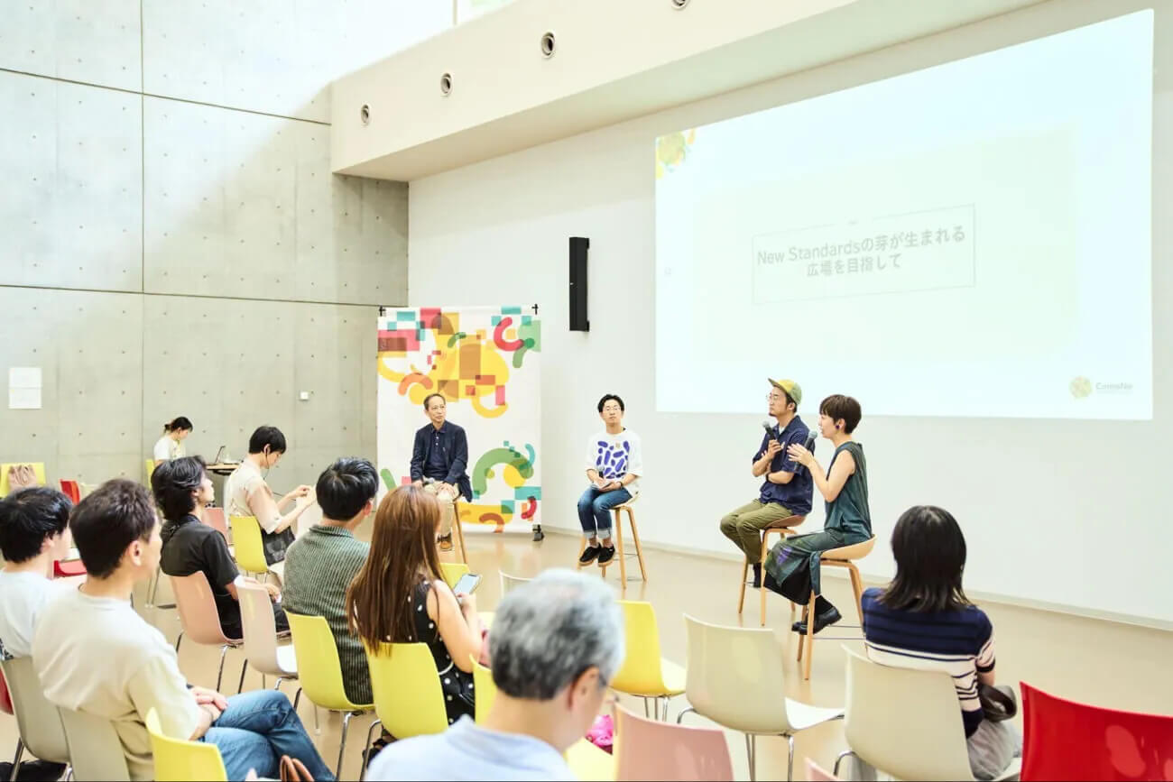 コモネで開催されたトークイベントの様子。会場前方で話す４人の登壇者の様子を、多くの観客が見守っている
