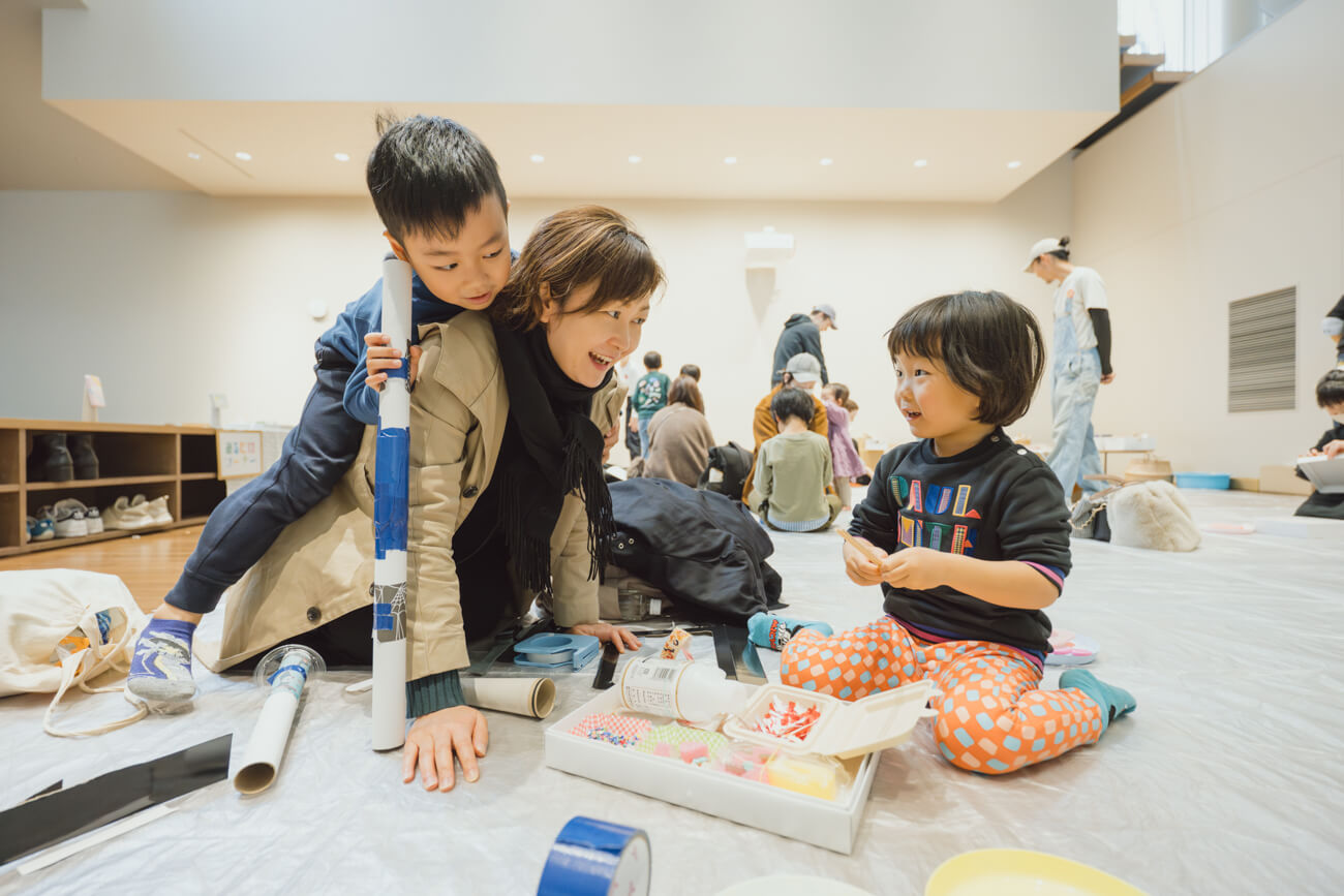 コモネで開催されたワークショップの様子。4~5歳くらいの子どもたちが手を動かして工作する様子を、一人の女性が子どもと同じ目線まで腰を下ろして見守っている