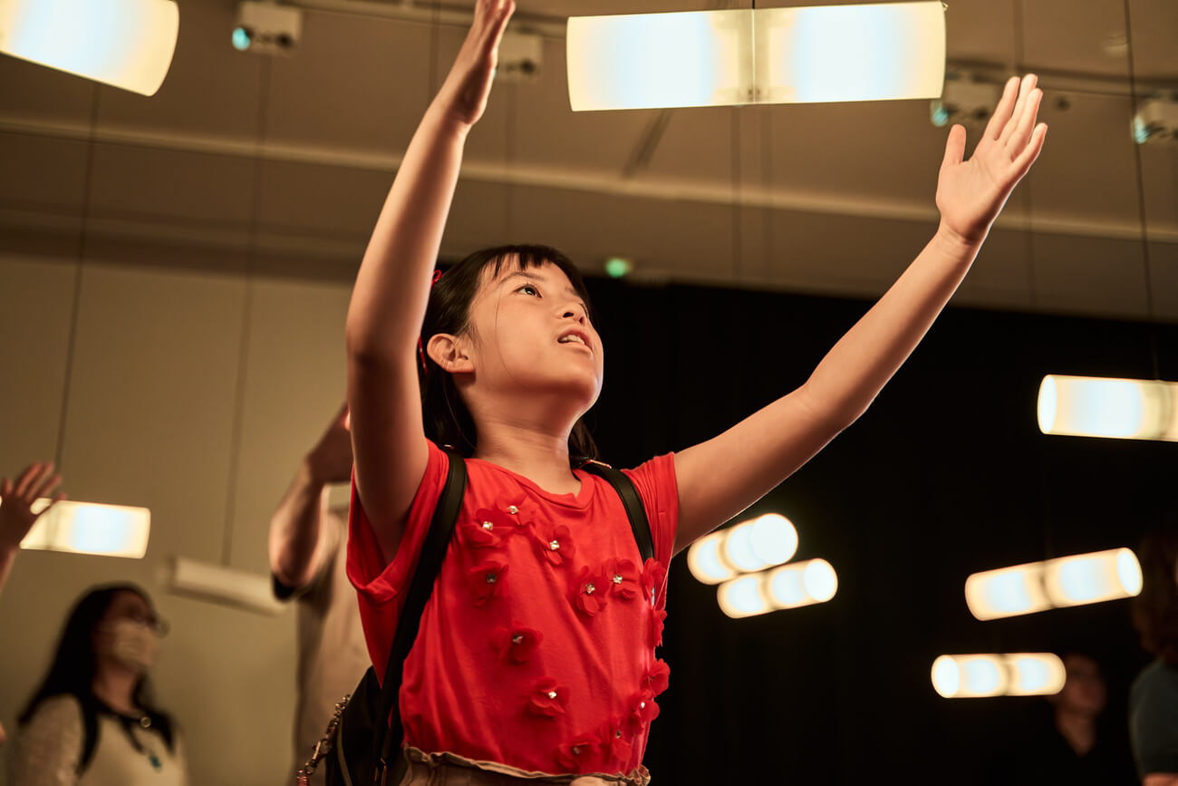 コモネ内にあるギャラリー「STEAM GALLERY」の体験展示に触れている子どもの写真。光る筒に手をかざし、作品が反応を起こすさまを見ている