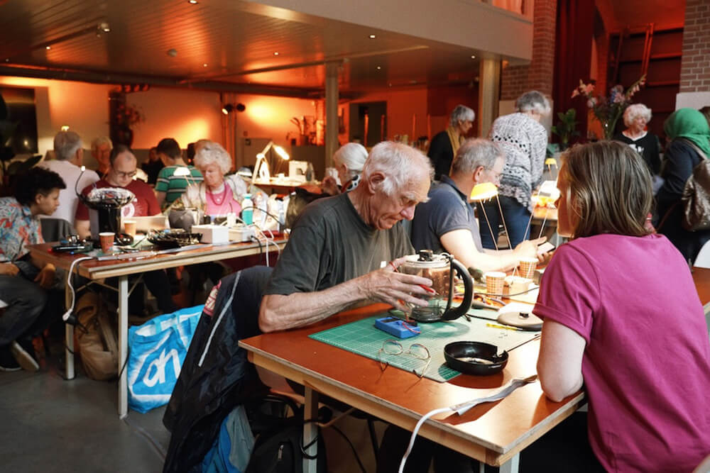 カフェに集まって、修理をしている人々の姿。老若男女が入り混じっている。