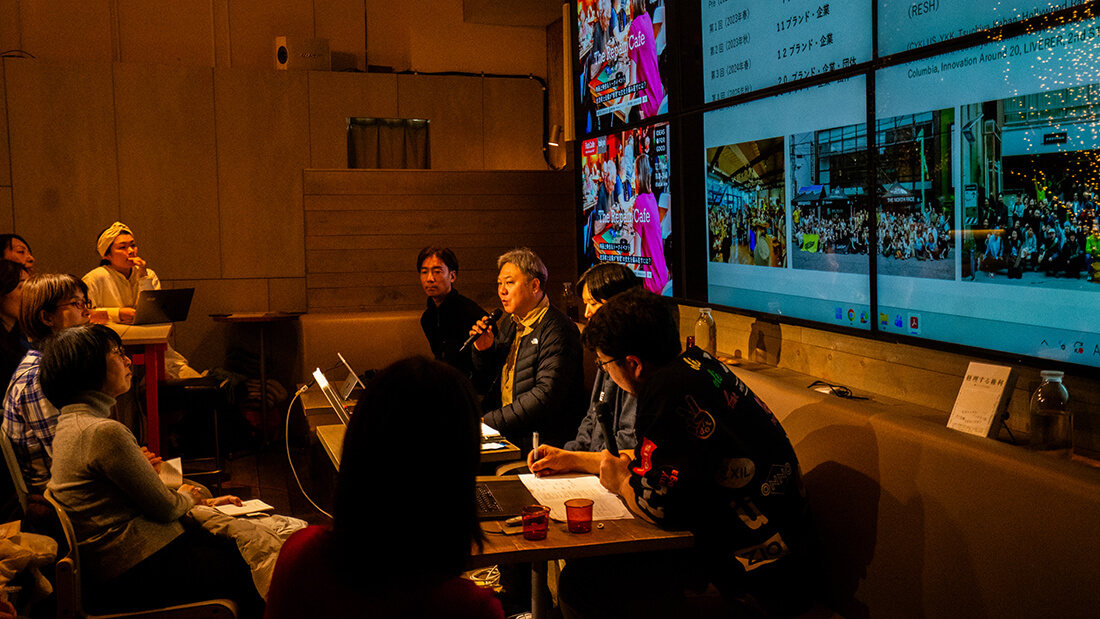 グレーヘアの男性、ゴールドウイン 畑野健一さん。マイクを持って客席に語りかけている。