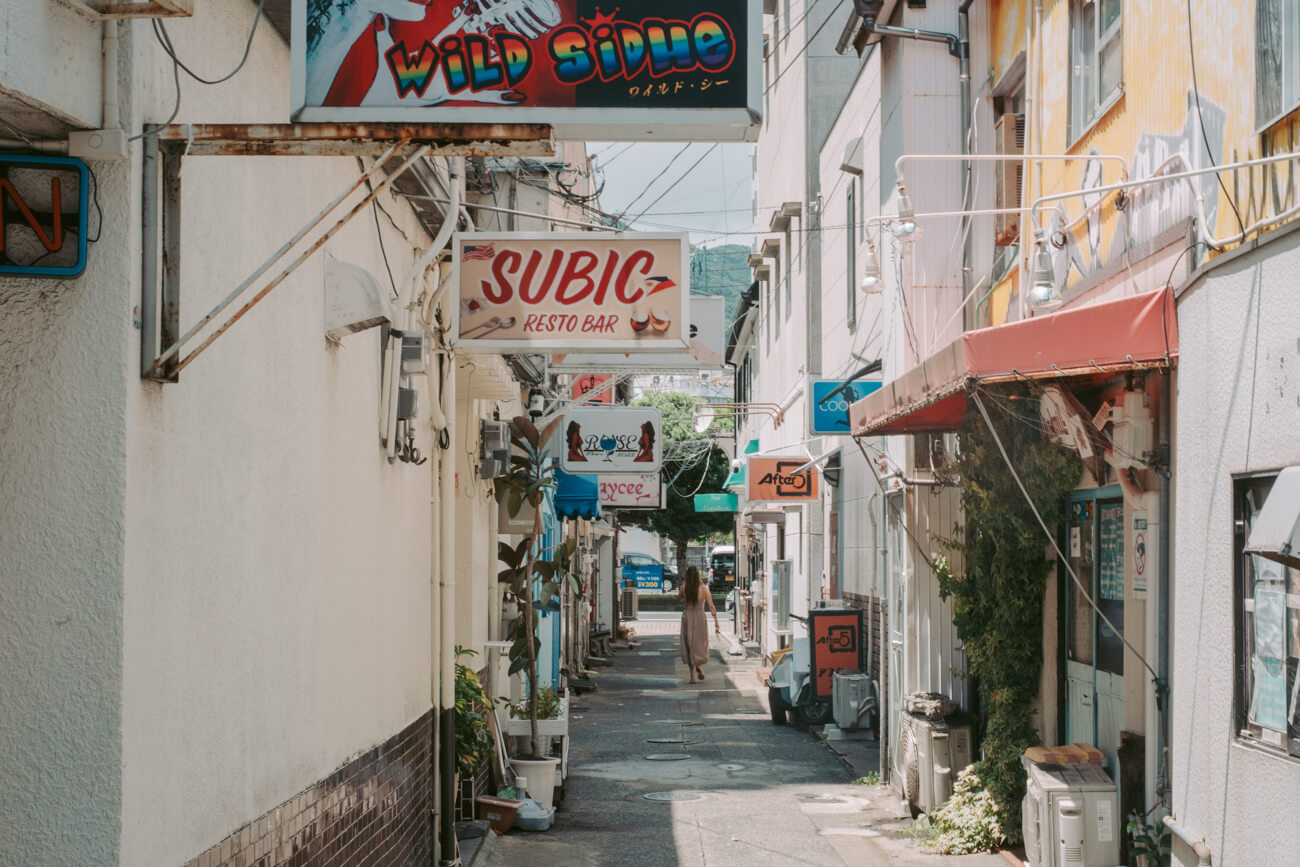 フィールドレコーディングが行われた、佐世保のまちなみの写真。昼間の細い路地にたくさんのバーの看板が並ぶ