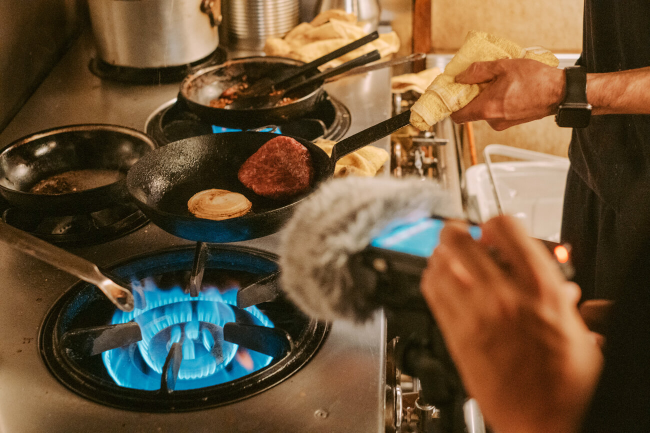 調理中の音を、フィールドレコーディングする写真。肉を炒めているフライパンに向かってレコーダーが向けられている