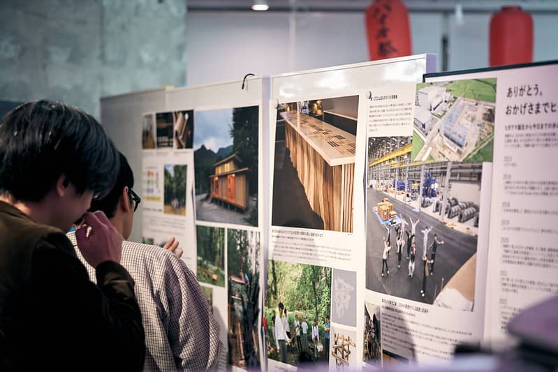 写真：展示パネルをじっくりと眺める参加者の様子。建築・空間・地域プロジェクトなど多様なビジュアルと言葉で構成されたパネルが並ぶ。