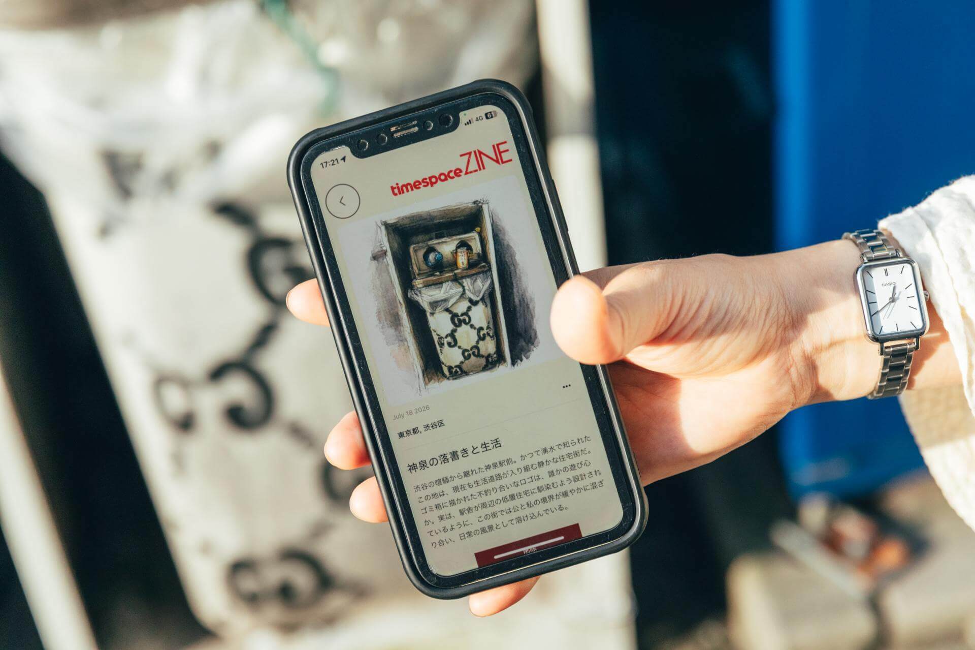 timespace ZINEが生成した記事の画面。日付は「July 18 2026」、場所は「東京都, 渋谷区」、見出しは「神泉の落書きと生活」。ゴミ箱にブランドロゴ柄の袋が収められた様子を描いたイラストと、かつて湧水で知られた神泉の住宅街について書かれた本文が並ぶ