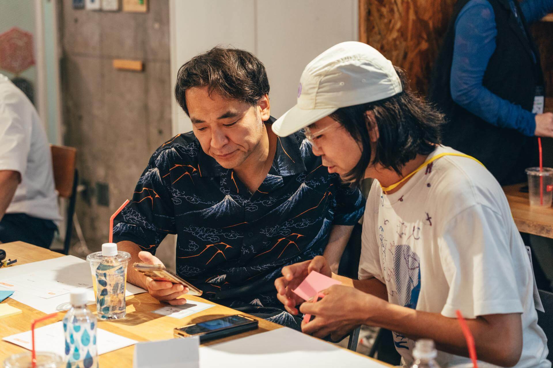 参加者2人が、撮影した写真をスマートフォンで見ながら、ピンクの付箋を手に話し合っている