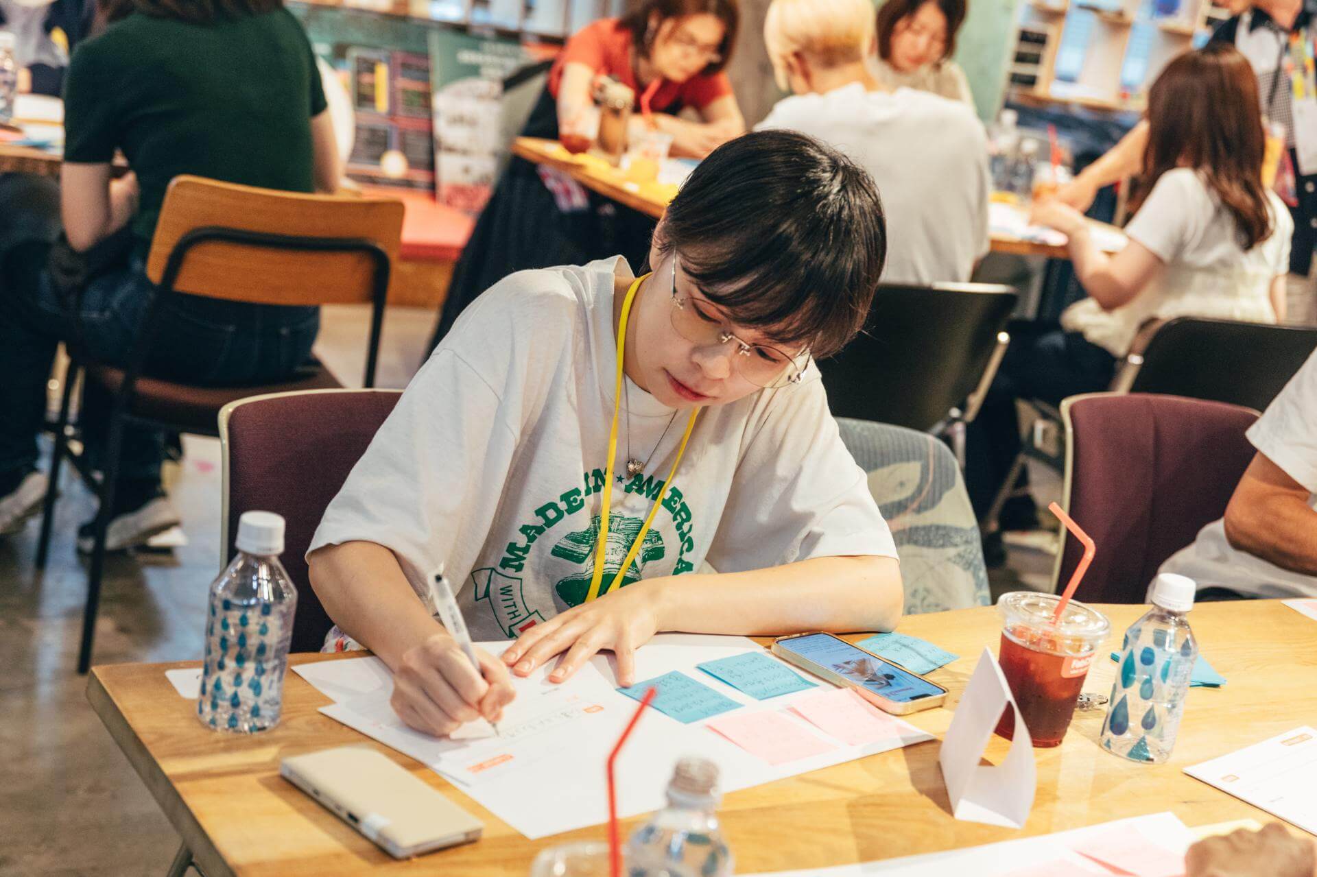 ワークシートにペンで書き込む参加者。手元には、手書きの文字で埋まった付箋とスマートフォンが並ぶ