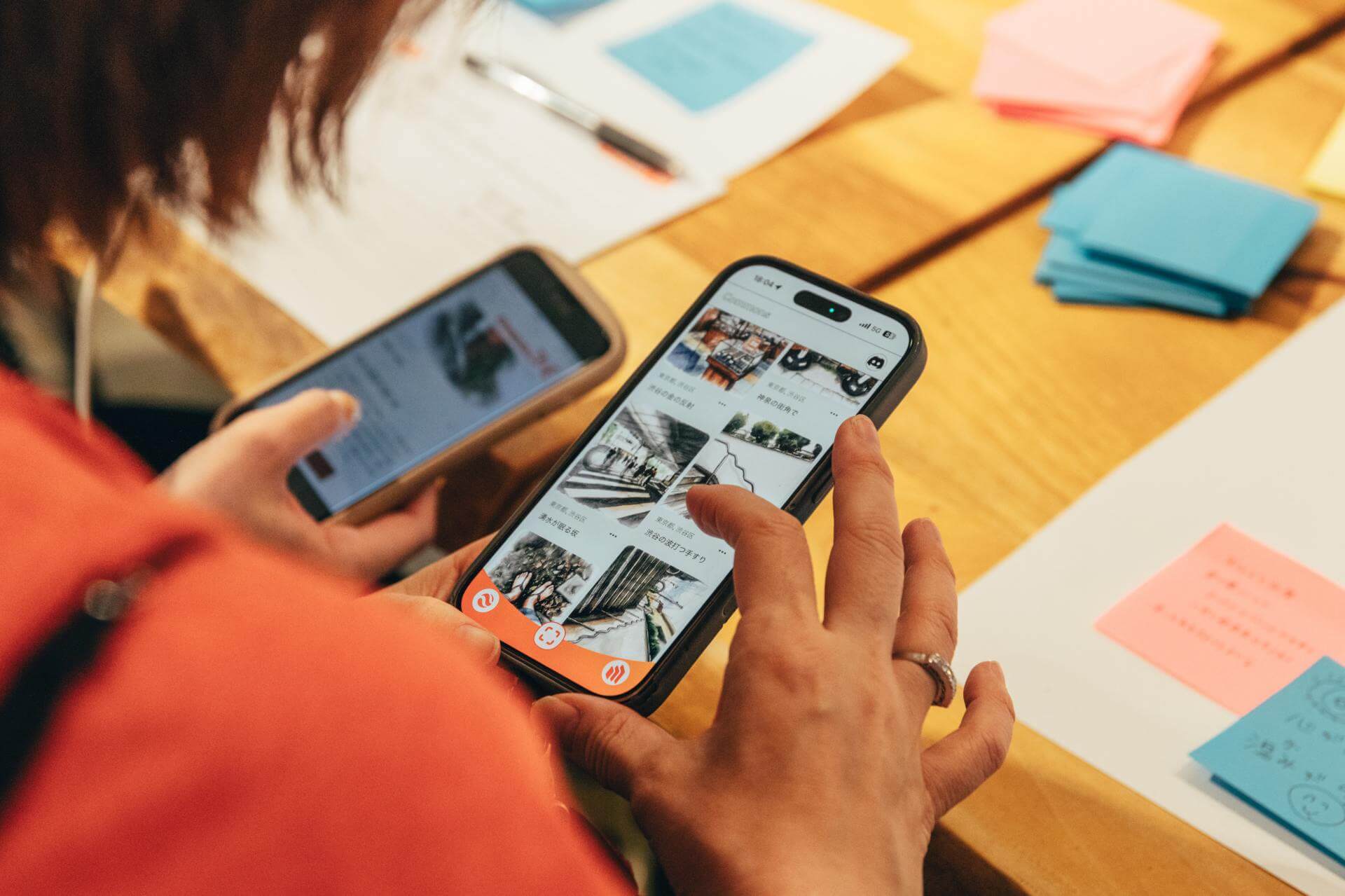 2台のスマートフォンを手に、timespace ZINEのCommons画面を見比べる参加者。「東京都, 渋谷区」で生成された記事が、「神泉の街角で」「湧水が眠る坂」「渋谷の波打つ手すり」といったタイトルで一覧に並ぶ