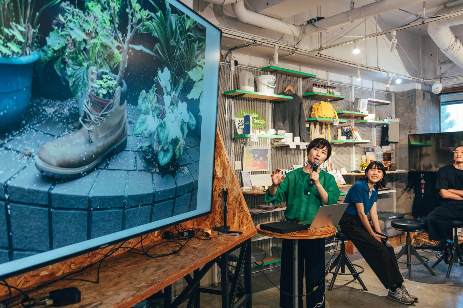 大型ディスプレイに、履き古したブーツを鉢代わりにして植物が育つ路上の植栽が映し出され、その前でマイクを持った登壇者が話している