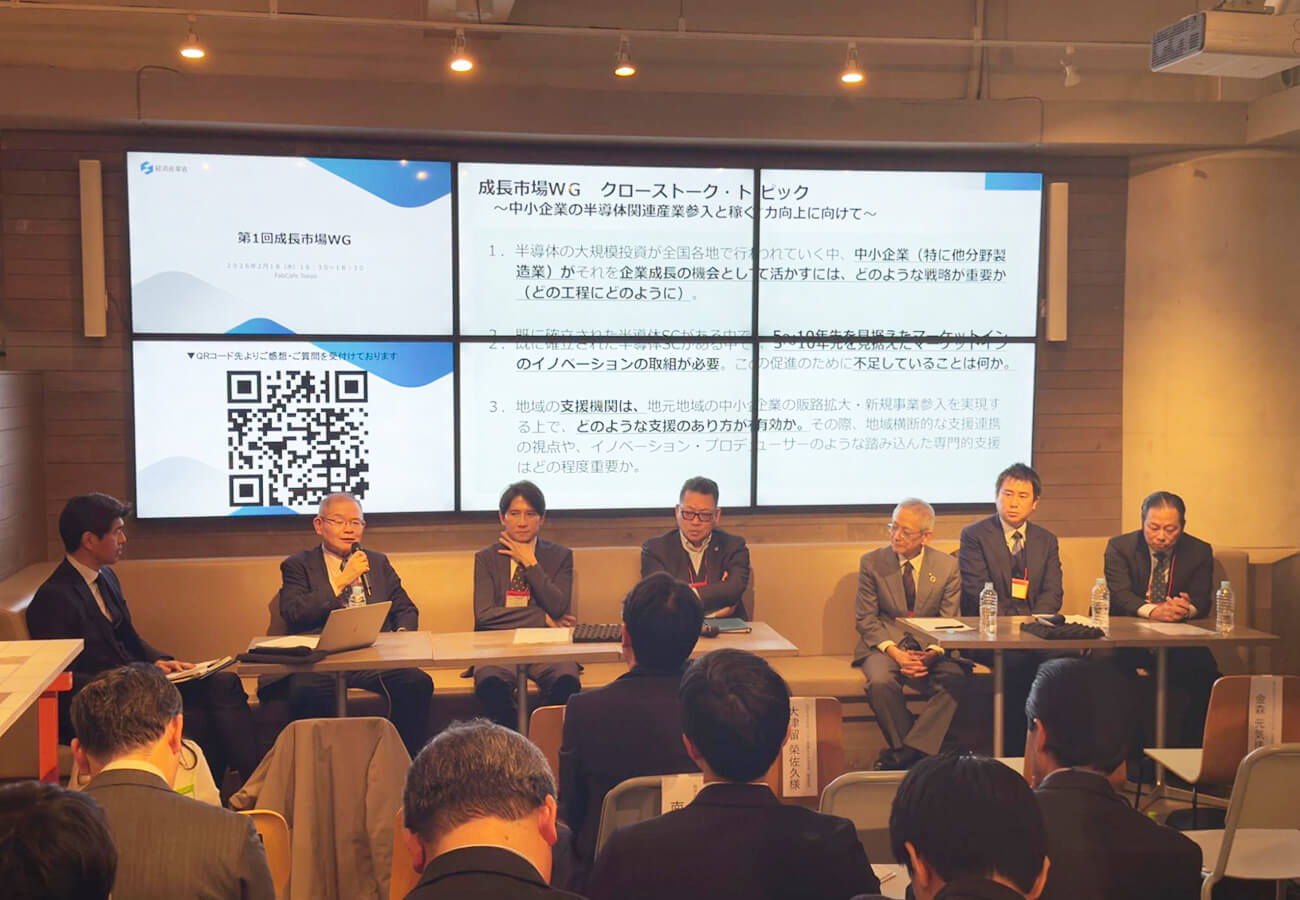 「第1回成長市場WG」でのクロストーク。スクリーンには「中小企業の半導体関連産業参入と稼ぐ力向上に向けて」と3つの論点が映され、並んで着席する登壇者7名のうち1名がマイクを持って話している。