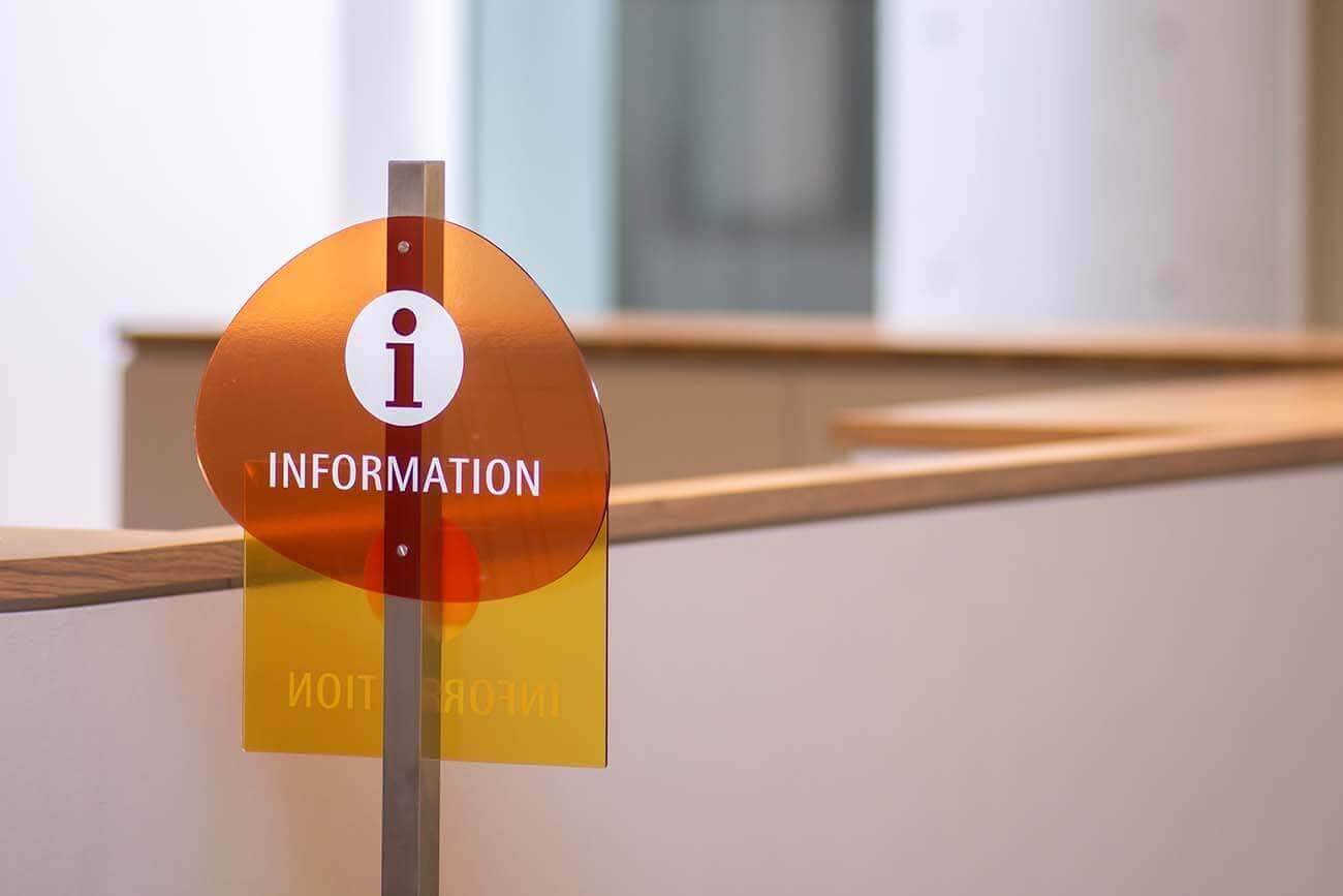 館内に設置されたインフォメーションサイン。オレンジと黄色の透明パネルに『i INFORMATION』と記されている。
